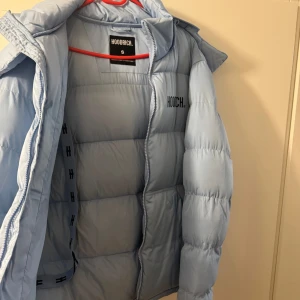 Ljusblå pufferjacka från Hoodrich - Snygg ljusblå pufferjacka från Hoodrich med broderad logga på bröstet och ryggen. Jackan har en avtagbar huva och dragkedja framtill. Perfekt för kyliga dagar. Den är ett halvår gammal och ny pris på den är 2000kr köpt från hoodrich pris kan diskuteras 