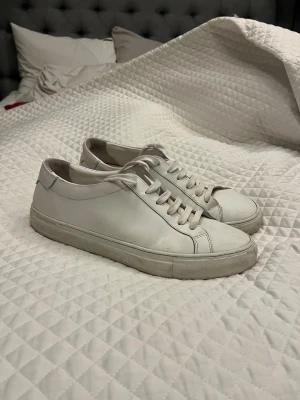 Vita sneakers från Polo Ralph Lauren - Snygga vita sneakers från Polo Ralph Lauren med stilren design och rund tå. Skorna är tillverkade i slätt skinn och har klassisk snörning framtill. Perfekta för dig som gillar minimalistisk och clean stil. Yttersulan är platt och ger en skön känsla hela dagen.