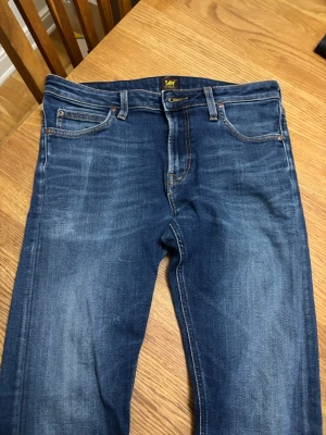 Blå Lee jeans med straight fit 31/32 - Snygga blå jeans från Lee med klassisk femficksdesign och brunt Lee-läderpatch bak. Jeansen har en rak passform och normal midja, tillverkade i slitstarkt denim med snygga tvättade detaljer. Perfekt för dig som gillar en tidlös och clean look.