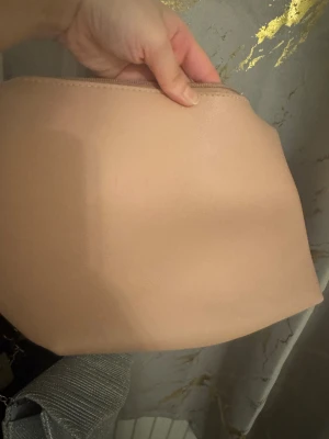 Beige kuvertväska i syntetmaterial - Enkel och stilren beige kuvertväska med dragkedja upptill. Väskan har en slät yta och är tillverkad i syntetmaterial, perfekt för att bära det viktigaste. Passar dig som gillar minimalistisk och clean stil.