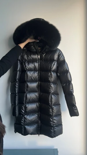 Dunjacka Colmar - Snygg svart dunjacka från Colmar med glansig finish och stor fluffig huva med päls. Längden på jackan når ner till mitten av låren. Storlek XS / 34(EU) / 40(IT)  Plagget är så gott som nytt, endast använt ett fåtal gånger. Nypris 8 500kr.