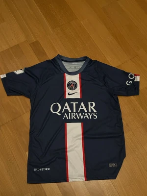 PSG Mbappé matchtröja Nike blå - Säljer en  Paris Saint-Germain matchtröja med Mbappé och nummer 7 på ryggen. Tröjan är marinblå med vit och röd rand framtill, PSG-logga på bröstet och Qatar Airways som sponsor. Perfekt för Psg fans! Står XL på tröjan men är perfekt för L