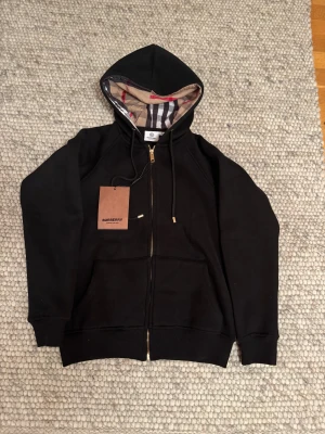 Burberry Hoodie  - Tjena, säljer nu en riktigt fet burberry zip hoodie som aldrig har använts innan. Köpt i butik och har prislapp kvar fortfarande. Storleken är S men jag skulle säga att den passar mellan XS och S beroende på vikt. Skriv gärna om ni har några funderingar👍👍