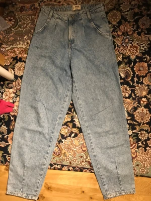 Ljusblå mom jeans från Denim Collection - Ljusblå mom jeans från Denim Collection i klassisk 90-talsstil. Hög midja, raka ben och avslappnad passform. Jeansen har två framfickor, två bakfickor och bälteshällor. Tillverkade i kraftigt denimtyg för en cool vintagekänsla.