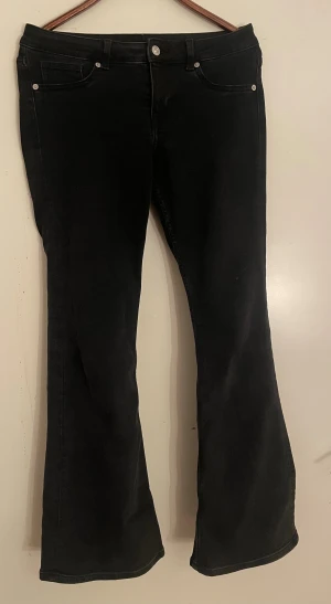 Svarta bootcut jeans med fickor - Snygga svarta jeans med bootcut passform och klassiska fem fickor. Byxorna har bälteshällor, knapp och dragkedja framtill. Materialet är jeans och färgen är helsvart, vilket ger en stilren och cool look. Perfekt för dig som gillar retrovibbar och markerade ben.