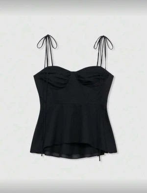 Svart linnetopp med knytband - Snygg svart linnetopp med tunna axelband som knyts i rosetter. Toppen har en lätt utsvängd nederdel och rynkade detaljer vid bysten för en feminin look. Perfekt för att styla med jeans eller kjol. Materialet känns lätt och luftigt.