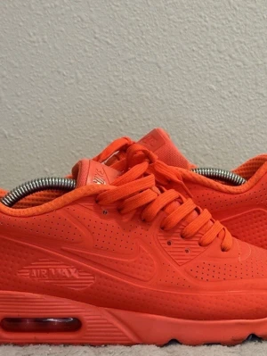 Nike Air Max 90 Ultra röd 44.5 - Nike Air Max 90 Ultra i helrött med snygg perforerad ovandel och klassisk Air Max-sula. Skorna har rund tå, snörning och är tillverkade i syntetmaterial och mesh för en sportig vibe. Perfekta för dig som vill sticka ut med färg på fötterna.