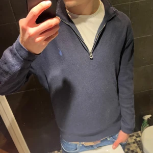 Marinblå half zip tröja Polo Ralph Lauren - Snygg marinblå tröja från Polo Ralph Lauren med half zip och klassisk broderad logga på bröstet. Tröjan är stickad i bomull och har långärmad passform med ribbade muddar. Perfekt för dig som gillar stilren och enkel design. Lite liten i storken, sitter mer som L enligt mig.