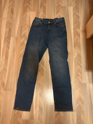 Blå jeans från Jack & Jones straight fit - Snygga blå jeans från Jack & Jones med klassisk femficksdesign och rak passform. Jeansen har en mörk tvätt med lätt slitning och detaljerad söm. Materialet är robust denim i bomull och de har normal midja. Perfekt för dig som gillar enkel och stilren look. Pris kan även diskuteras 