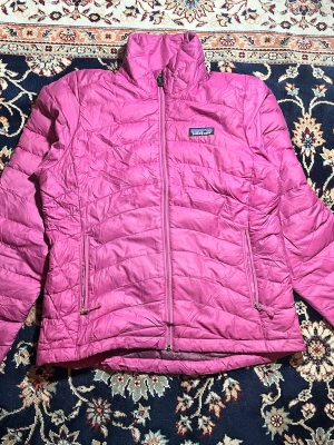 Rosa dunjacka från Patagonia XS 🌸 - Säljer en snygg rosa dunjacka från Patagonia i storlek XS. Jackan har quiltad design, hög krage och två praktiska fickor med dragkedja. Perfekt för kyliga dagar och har en lätt, smidig passform. Fodret är mörkare rosa och jackan stängs med dragkedja framtill.
