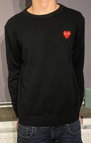 Svart tröja från Comme des Garçons - Svart stickad tröja från Comme des Garçons PLAY med ikoniskt rött hjärta på bröstet. Rund hals och långa ärmar. Storlek L men passar bättre som storlek M