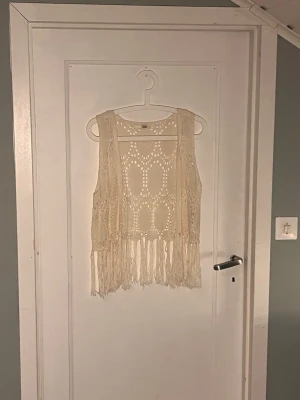 Festival style väst från ONLY - Säljer en beige stickad väst från ONLY i storlek L. Västen har ett snyggt virkat mönster och långa fransar längs nederkanten som ger boho-vibes. Perfekt att slänga över en t-shirt eller klänning för en chill look.