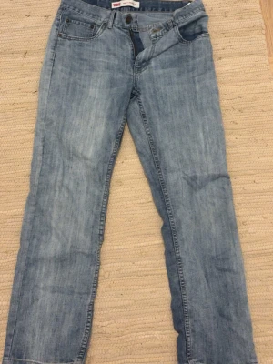 Levis 505 ljusblå jeans straight fit - Ljusblå Levis 501 jeans med klassisk straight fit och fem fickor. Jeansen har en knappgylf, Levis patch bak och den ikoniska röda Levis-taggen på bakfickan. Tillverkade i slitstarkt denim med en lätt tvättad look.