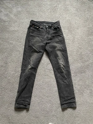 Levi's 501 svarta jeans straight fit - Säljer ett par klassiska Levi's 501 jeans i svart tvättad denim. Modellen har rak passform, fem fickor och knappgylf. Snyggt slitna detaljer och ikonisk läderpatch bak i midjan. Perfekta för en avslappnad och tidlös look.