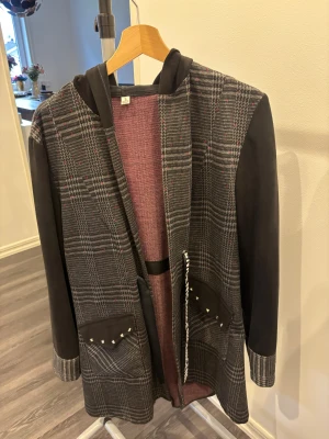 Rutig overshirt med huva och snörning - Snygg overshirt med huva i mörkgrått och rutig design med diskreta röda detaljer. Jackan har svarta ärmar, coola fickor med nitar och en snörning med texten NICE. Perfekt för dig som gillar streetstyle och vill sticka ut lite extra.