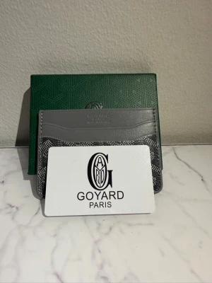 Grå kortfodral i läder - Snyggt och stilrent kortfodral i grått läder med klassiskt mönster och flera kortfack. Perfekt för dig som vill ha en exklusiv accessoar med ikonisk design. Kompakt format som passar i fickan och ger en lyxig känsla.