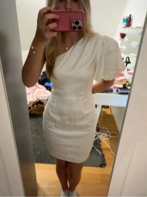 Vit studentklänning - Säljer en vit kortklänning från NA-KD med oneshoulder-design och puffärm. Klänningen har en figurnära passform och är tillverkad i ett slätt material som ger en elegant look. Perfekt till studenten och midsommar, aldrig använt den!! 