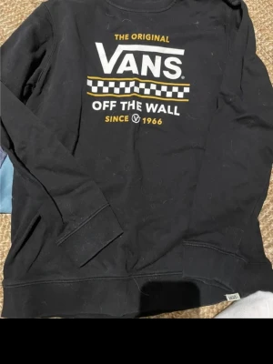 Svart Vans sweatshirt XL - Svart sweatshirt från Vans med trycket 'The Original Vans Off The Wall Since 1966' i vitt och gult på bröstet. Klassisk crewneck-modell med ribbade muddar vid ärmslut och nederkant. Perfekt för en avslappnad streetwear -look.   Skulle säga att den är mer S-M i storleken