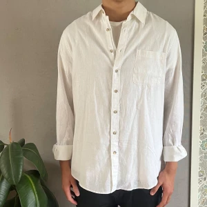 Vit linneskjorta från Dressmann - Säljer en klassisk vit skjorta från Dressmann i linnemix, perfekt för sommaren. Skjortan är helt oanvänd! Den har lång ärm, bröstficka och knäppning framtill. Perfekt för en stilren och avslappnad look. Passar dig som gillar enkel och tidlös stil.