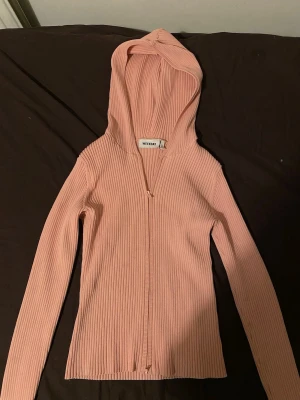 Rosa ribbad hoodie från Weekday - Säljer en ljusrosa ribbad hoodie från Weekday med dragkedja framtill och långa ärmar. Hoodien har en smal passform och är tillverkad i ett stretchigt material som sitter snyggt på kroppen. Perfekt för en chill och stilren look.