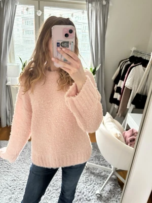 Ljusrosa fluffig stickad tröja - Supermjuk och oversized ljusrosa stickad tröja med breda ärmar och ribbade muddar. Perfekt för att mysa i under kyliga dagar. Tröjan har en enkel, klassisk design och är gjord i ett fluffigt material som känns riktigt skönt mot huden.