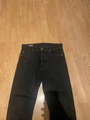 Svarta straight jeans från G-Star RAW - Snygga svarta jeans från G-Star RAW, modell 3301 Straight. Klassisk femficksdesign med raka ben och normal midja. Perfekta för dig som gillar en stilren och enkel look. Materialet är denim med en mjuk känsla. Lite sönder vid sidan därav priset.