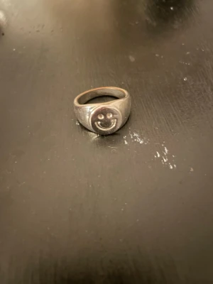 Silverring med smiley - Stilren silverring med en smiley. Ringen har en klassisk och elegant design med slät silverfärgad ring och en centralt placerad smiley. Perfekt för dig som gillar tidlösa smycken med en touch av lyx.