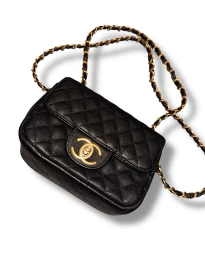 Chanel svart quiltad axelväska - Snygg svart axelväska från Chanel i klassisk quiltad design med guldfärgade detaljer och kedjerem. Väskan är tillverkad i läder och har det ikoniska CC-spännet framtill. Perfekt för dig som vill ha en tidlös och lyxig accessoar. (Väskan är köpt på second hand så vet inte alls värde med mera)