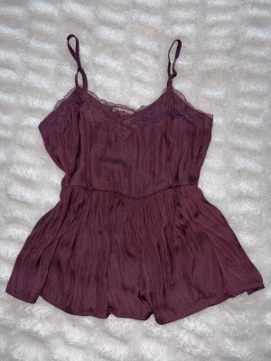 Vinröd topp med spetsdetaljer - Söt vinröd topp med tunna axelband och spetsdetaljer vid ringningen. Toppen har en flowy passform och är tillverkad i ett lätt, luftigt material som passar perfekt till sommaren. Perfekt att styla med jeans eller kjol för en trendig look. Från Anna Field och i väldigt bra skick. Storlek S