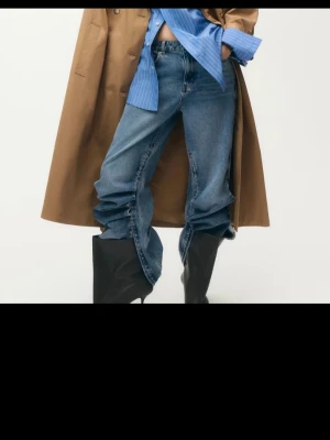 Blå wide jeans med slitsdetalj - Trendiga blå jeans med bred passform och coola slitsar längs benen. Jeansen har klassisk femficksdesign och är tillverkade i denim. Perfekta för dig som vill sticka ut med en unik look.