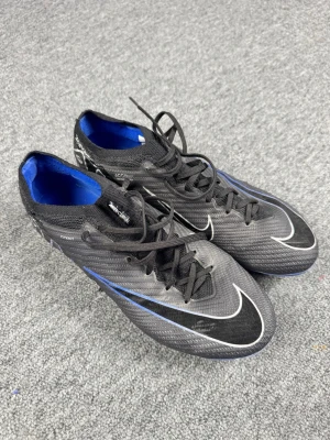 Nike Mercurial svart/blå fotbollsskor - Säljer ett par Nike Mercurial fotbollsskor i svart med blå och vita detaljer. Skorna har snörning, låg profil och syntetiskt material för lätt vikt och bra bollkontroll. Yttersulan har fasta dobbar och Air Zoom-dämpning för extra komfort på planen.