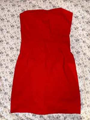 Röd tube kort klänning - Snygg röd axelbandslös kort klänning med figurnära passform. Klänningen har en liten slit på baksidan.
