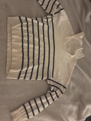 Beige  stickad tröja med svarta ränder  - Snygg vit stickad tröja med marinblå horisontella ränder och ribbstickade muddar. Tröjan har lång ärm och klassisk rund halsringning. 