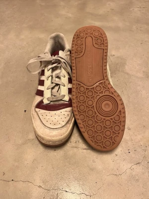 Adidas sneakers med vinröda detaljer - Snygga Adidas sneakers i vitt med vinröda detaljer. Sparsamt använda.