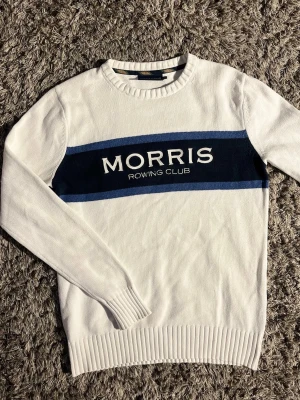 Vit tröja från Morris🙌🤩 - Snygg vit stickad tröja från Morris Rowing Club med blått band och logga över bröstet. Tröjan har rund halsringning, ribbade muddar och är perfekt för en clean och sportig stil.🙌🤩