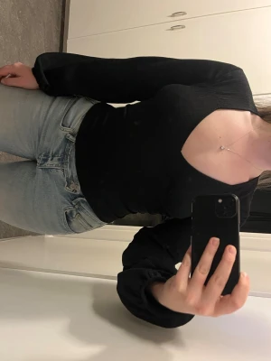 Svart långärmad topp med öppen rygg - Trendig svart långärmad topp med djup urringning framtill och öppen rygg med knytband. Figurnära passform och stretchigt material.