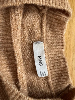 Ljus brun stickad tröja från Mango  - Mysig ljus brun stickad tröja från mango  med klassisk rund hals och långa ärmar. Tröjan har ribbade muddar vid ärmslut och nederkant, perfekt för lager på lager under höst och vinter. Enkel och stilren design som passar till allt. Liten fläck på ärmen men syns inte riktigt!! 