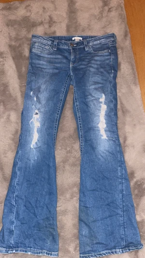 Ljusblåa jeans med hål vid knäna gina tricot - Väldigt snygga ljusblå jeans de är väldigt låg midjade och kanappt använda de har fickor men knapp baktill 