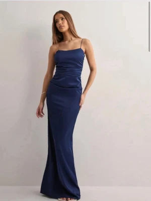 Marinblå balklänning med smala axelband - Säljer min balklänning med smala axelband och öppen rygg. Endast använd en gång och den är perfekt till bal, bröllop, fester osv. Den har en mörk fläck på baksidan syns knappt då den är mycket mörk, kontakta för bilder på det. Priset går att diskutera vid snabb affär💗