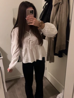 Vit blus i en stilren och tidlös design. Tillverkad i ett lätt och bekvämt material som passar både vardag och finare tillfällen. Enkel att matcha med både byxor och kjol för en klassisk och elegant look. - Vit blus med dekorativa rosetter framtill som ger ett elegant och feminint uttryck. Blusen har en stilren design och är tillverkad i ett lätt och behagligt material som faller snyggt. Passar perfekt både till vardags och till mer uppklädda tillfällen.