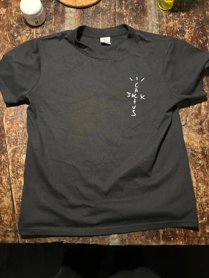 Svart Cactus Jack Rodeo t-shirt - Svart t-shirt från Cactus Jack med tryck på både fram- och baksidan. Framsidan har ett litet vitt Cactus Jack-tryck, medan baksidan har ett stort motiv med skelett, röd text 'RODEO' och detaljerad grafik. Rund hals och korta ärmar, tillverkad i mjuk bomull.