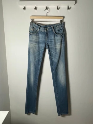Blå raka jeans från KAPORAL - Säljer ett par ljusblå jeans från KAPORAL med snygg slitning och raka ben. Jeansen har klassiska fem fickor, cool broderad logga på myntfickan och detaljerade bakfickor med läderpatch. Perfekta till vardags för en avslappnad look. Lågmidjade