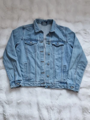 Ljusblå jeansjacka från Tom & Rose - Klassisk ljusblå jeansjacka från Tom & Rose med knappar framtill, två bröstfickor med lock och knapp samt sidofickor. Jackan har en rak passform och långa ärmar med knapp vid ärmslut. Perfekt att slänga över en hoodie eller t-shirt.