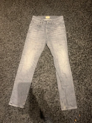 Grå slim jeans från Jack and Jones 29/32 - Snygga grå jeans från Jack and Jones i slim fit med klassisk femficksdesign och dragkedjegylf. Jeansen har en ljusgrå tvätt och raka ben, perfekta för en clean och stilren look. Tillverkade i mjukt jeanstyg som sitter tajt men ändå bekvämt. Hör av dig vid minsta fundering eller fråga pris kan även diskuteras! 💯