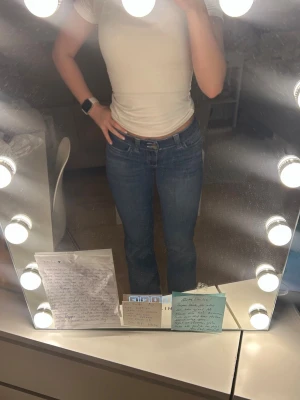 Blå jeans med strassdetalj bakficka - Säljer ett par blå jeans med snygg strassdetalj på bakfickan. Jeansen har låg midja och klassisk femficksmodell. De är raka i modellen och har en stilren look som passar till det mesta. Materialet är jeans och färgen är en mellanblå tvätt.