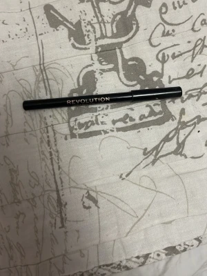 Svart eyeliner från Revolution - Säljer en svart eyeliner från Revolution med stilren design. Pennan är smal och enkel att använda för att skapa skarpa linjer. Perfekt för dig som vill ha en klassisk svart look. Snygg guldig text på hylsan.