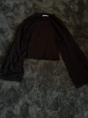 Svart långärmad topp - En svart långärmad topp från lager157. Toppen har en enkel och clean design med raka linjer och vida ärmar. Tillverkad i mjukt bomullsmaterial som känns skönt mot huden. Perfekt att styla med höga jeans eller kjol.