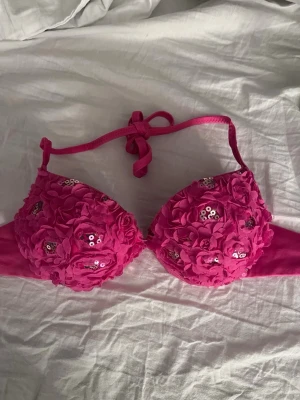 Rosa blommig bikiniöverdel med paljetter - Säljer en rosa bikiniöverdel med blommor och paljettdetaljer på kuporna. Överdelen har knyt i nacken och vadderade kupor för extra stöd. Köpte på plick men passade ej mig 💘