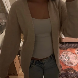 Stickad kofta - Mysig beige stickad kofta med lång ärm och öppen framtill. Koftan har en loose och oversized passform som gör den perfekt att slänga över en topp eller t-shirt. Enkel och stilren design utan knappar eller dragkedja.