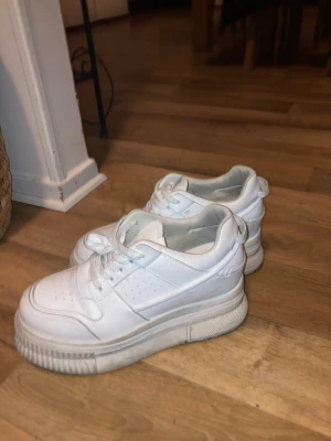 Vita chunky sneakers med plattform - Säljer ett par vita chunky sneakers från H&M med plattformssula och klassisk snörning. Skorna har perforerade detaljer på sidan och en rund tå. Tillverkade i syntetmaterial och passar perfekt till en streetwear-look.
